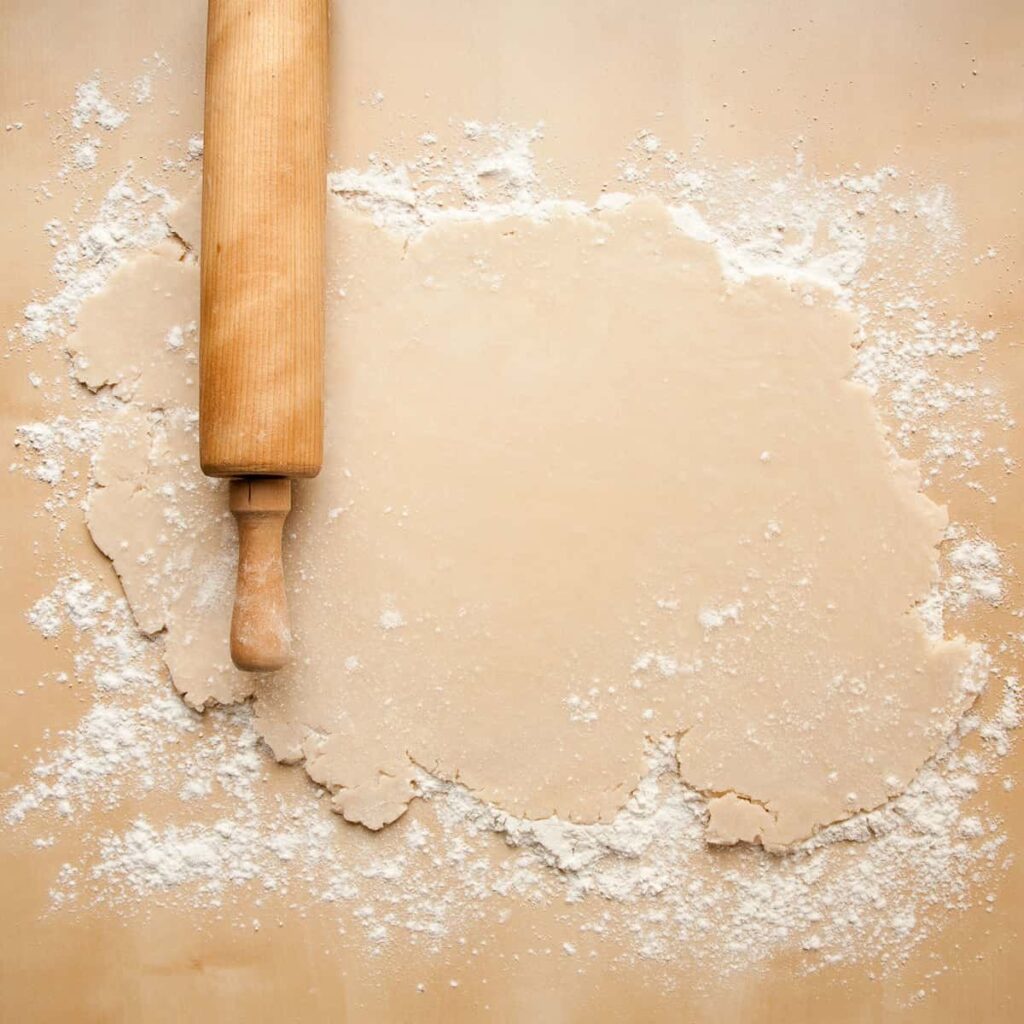 rolling pin and pastry dough on a kitchen counter, a baking tool close to 17 inches long